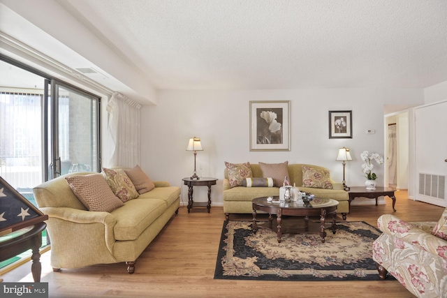 living area with light wood finished floors, visible vents, and a textured ceiling