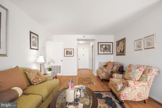 living room with light wood finished floors, baseboards, visible vents, and a textured ceiling