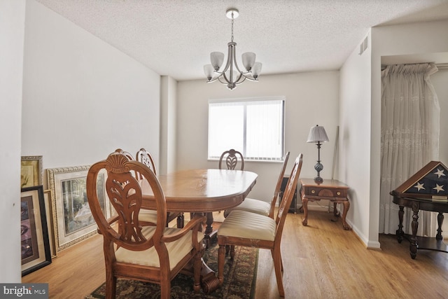 dining space featuring baseboards, visible vents, a textured ceiling, light wood-style floors, and a chandelier