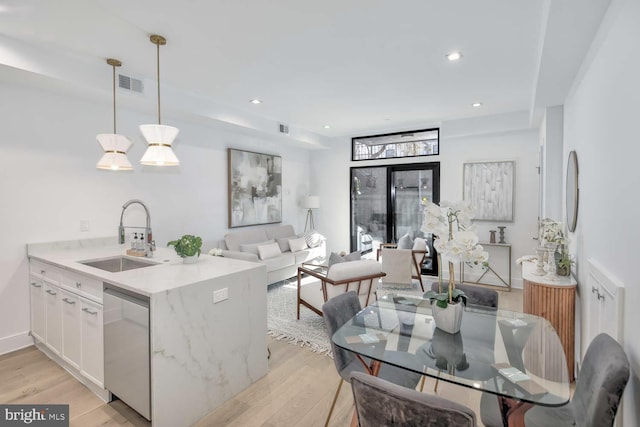 kitchen with pendant lighting, sink, dishwasher, white cabinetry, and light stone counters