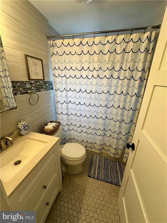 bathroom with curtained shower, tile walls, tile patterned flooring, vanity, and toilet