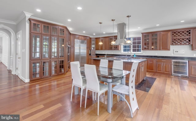 kitchen with pendant lighting, an island with sink, wine cooler, built in refrigerator, and island exhaust hood