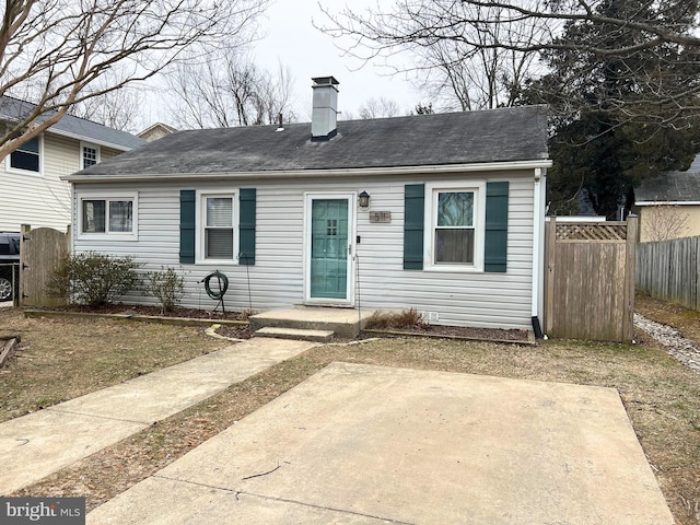 view of front of house with a shingled roof, a chimney, and fence