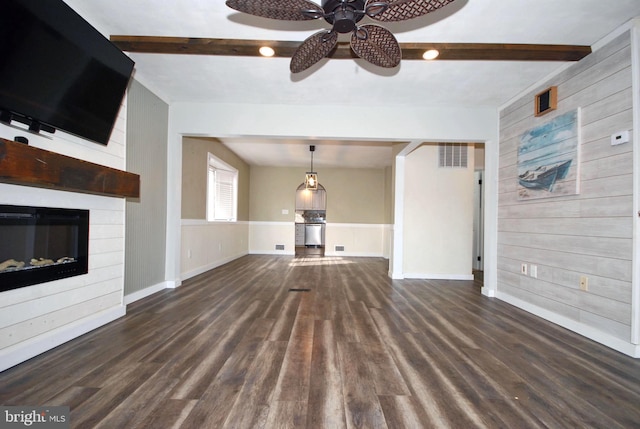 unfurnished living room featuring wooden walls, dark wood-style flooring, and beam ceiling