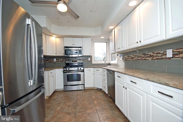 kitchen featuring appliances with stainless steel finishes, white cabinets, a sink, and light stone countertops