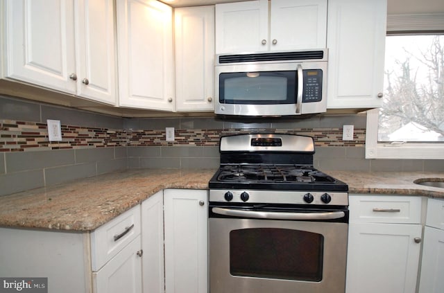 kitchen with stainless steel appliances, light stone counters, backsplash, and white cabinets