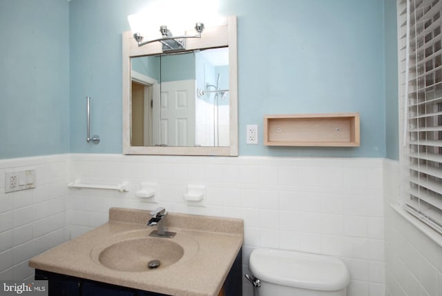 bathroom with tile walls, a wainscoted wall, vanity, and toilet