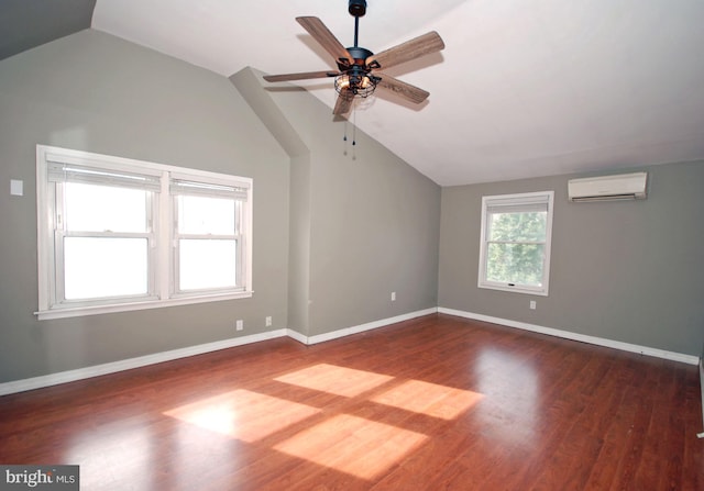 empty room featuring dark wood-type flooring, a wall unit AC, vaulted ceiling, and baseboards