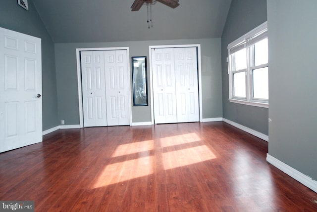 unfurnished bedroom featuring vaulted ceiling, two closets, and dark wood finished floors