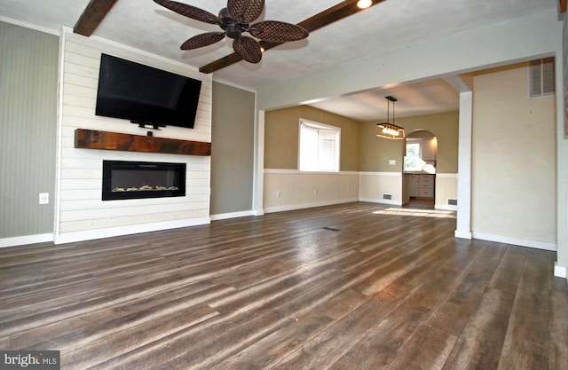 unfurnished living room featuring a large fireplace, arched walkways, dark wood finished floors, and a ceiling fan