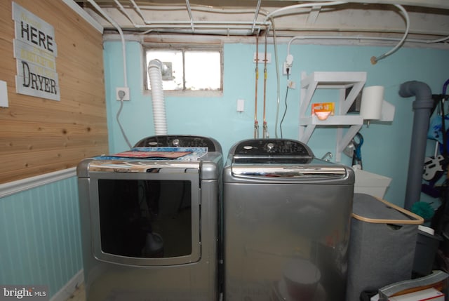 clothes washing area featuring laundry area, wood walls, and washing machine and clothes dryer