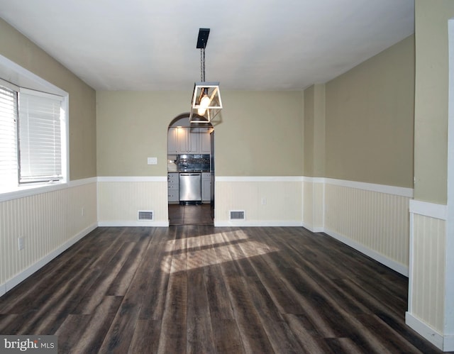 unfurnished dining area with arched walkways, wainscoting, dark wood finished floors, and visible vents