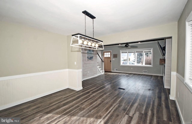 unfurnished dining area featuring dark wood-style floors, stairway, wainscoting, and visible vents