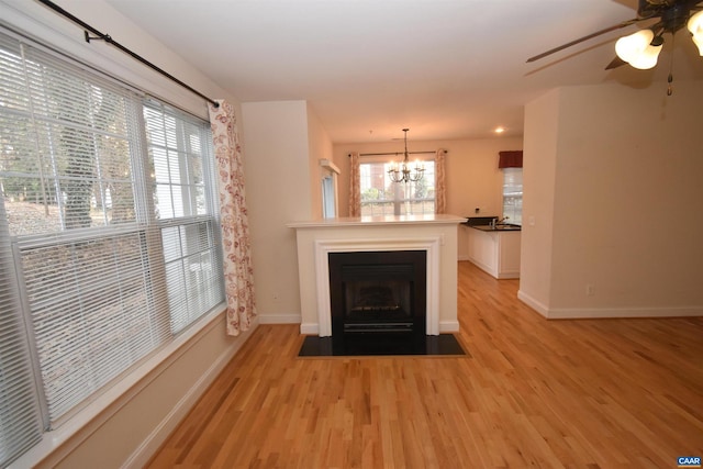 unfurnished living room featuring ceiling fan with notable chandelier, a wealth of natural light, and light hardwood / wood-style floors