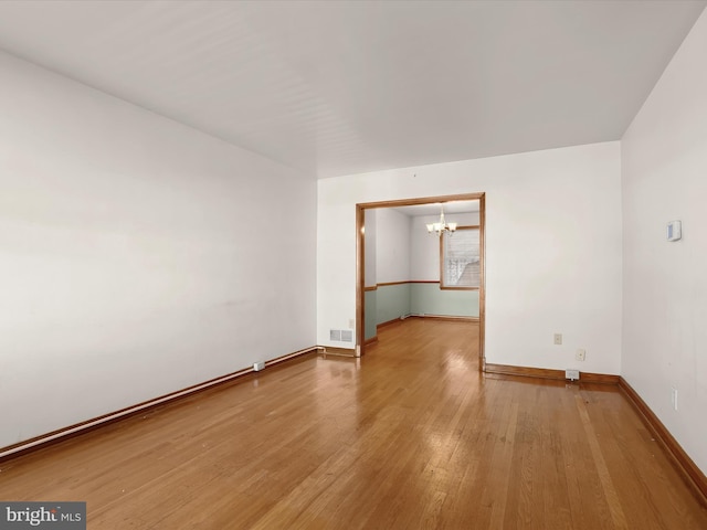 spare room with hardwood / wood-style flooring and a notable chandelier