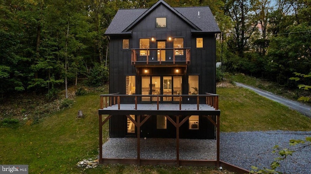 rear view of property with a balcony, a deck, and a lawn