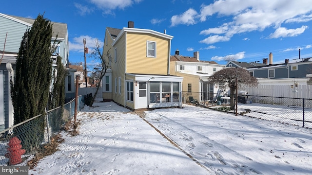 snow covered back of property featuring a sunroom