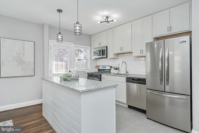 kitchen with sink, hanging light fixtures, stainless steel appliances, light stone countertops, and white cabinets