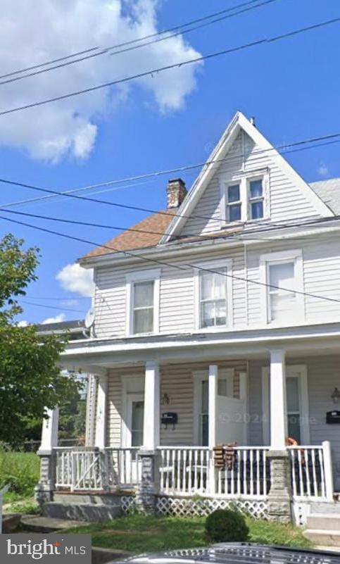 american foursquare style home featuring a chimney and covered porch