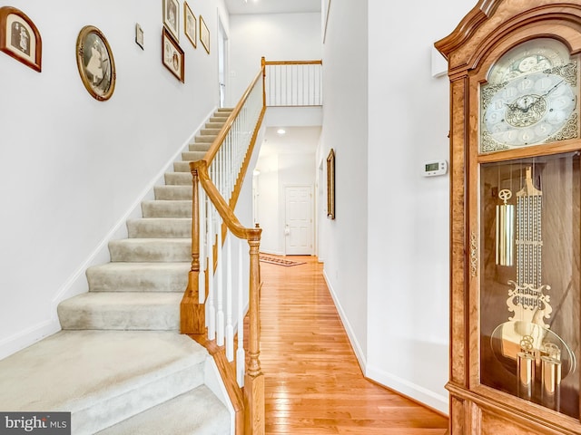 staircase with wood finished floors, a towering ceiling, and baseboards