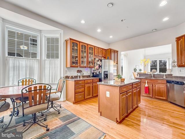 kitchen with a center island, stainless steel appliances, glass insert cabinets, a sink, and light stone countertops