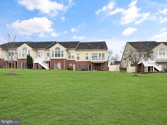 rear view of property featuring brick siding, stairway, and a yard