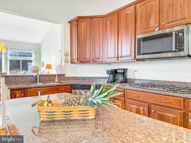 kitchen with dark stone counters, lofted ceiling, brown cabinets, stainless steel appliances, and a sink