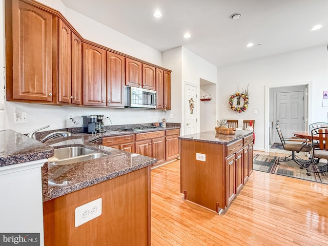 kitchen with appliances with stainless steel finishes, brown cabinets, a sink, and light wood finished floors