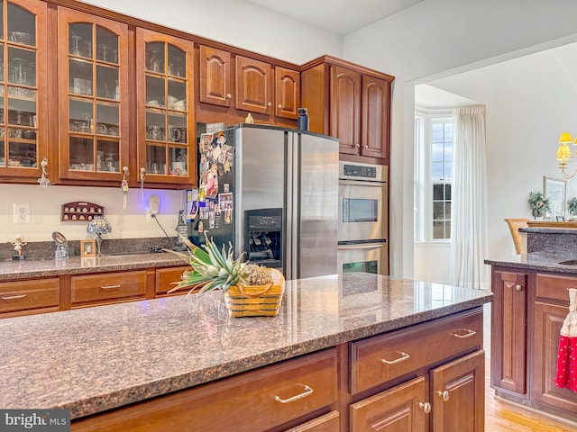 kitchen featuring glass insert cabinets, stone counters, appliances with stainless steel finishes, and brown cabinets