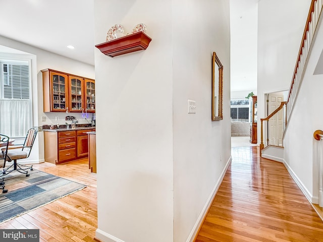 hallway with light wood-style flooring, recessed lighting, a towering ceiling, baseboards, and stairs