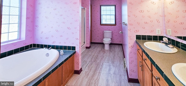 bathroom with a garden tub, toilet, a sink, double vanity, and wallpapered walls