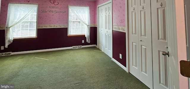 unfurnished bedroom featuring wallpapered walls, visible vents, dark colored carpet, and wainscoting