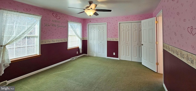 unfurnished bedroom with wallpapered walls, visible vents, baseboards, carpet flooring, and multiple closets