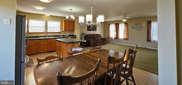 dining room featuring a healthy amount of sunlight, light carpet, baseboards, and ceiling fan with notable chandelier