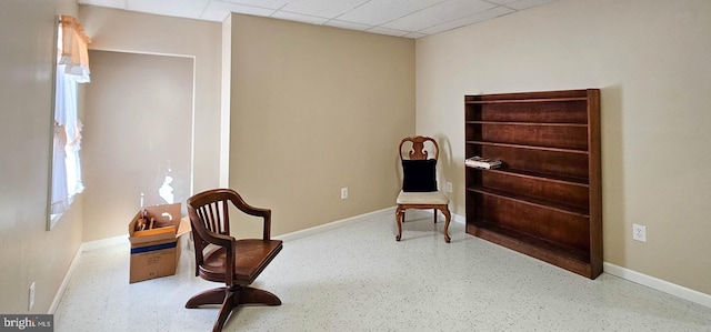 sitting room featuring a drop ceiling and baseboards