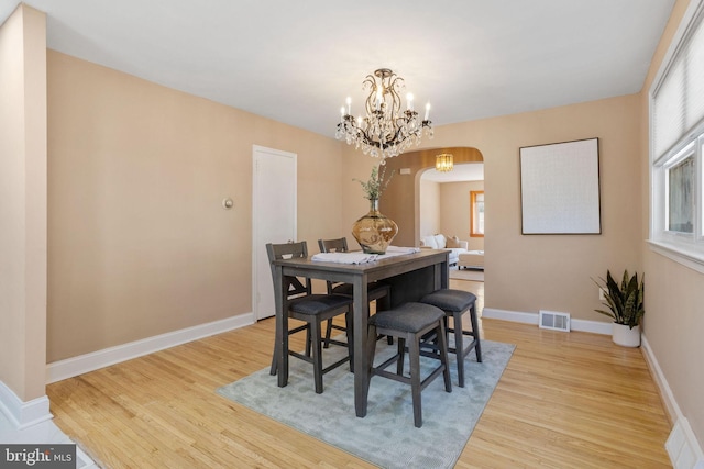 dining space featuring visible vents, arched walkways, light wood-style floors, baseboards, and a chandelier