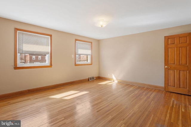 empty room with light wood-type flooring, visible vents, and baseboards