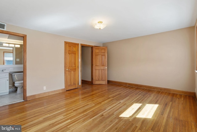 unfurnished bedroom with connected bathroom, baseboards, light wood-style floors, and visible vents