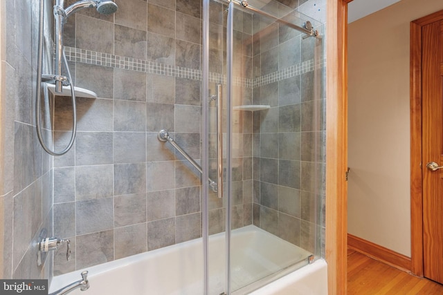 bathroom featuring wood finished floors, baseboards, and bath / shower combo with glass door