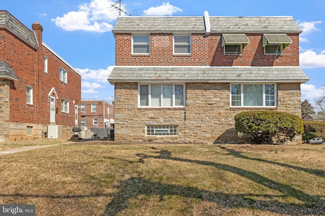 rear view of property with a lawn, stone siding, and roof with shingles