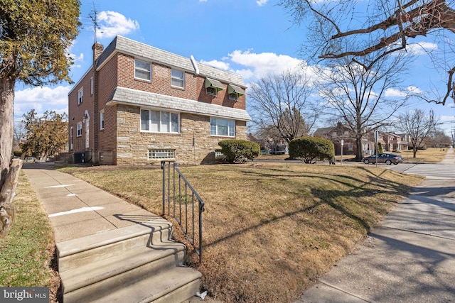 view of front of property featuring a front yard, a chimney, stone siding, central air condition unit, and brick siding