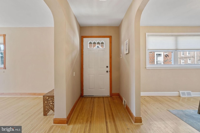 foyer with visible vents, arched walkways, baseboards, and wood finished floors