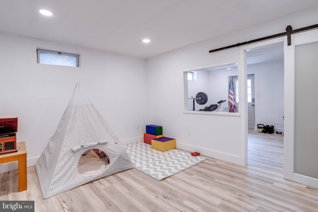 recreation room featuring light wood-type flooring and a barn door