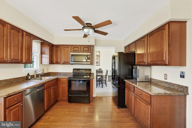 kitchen featuring light hardwood / wood-style flooring, black appliances, sink, ceiling fan, and dark stone countertops