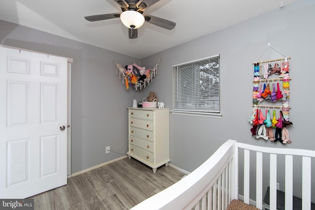 bedroom featuring a ceiling fan, a nursery area, baseboards, and wood finished floors