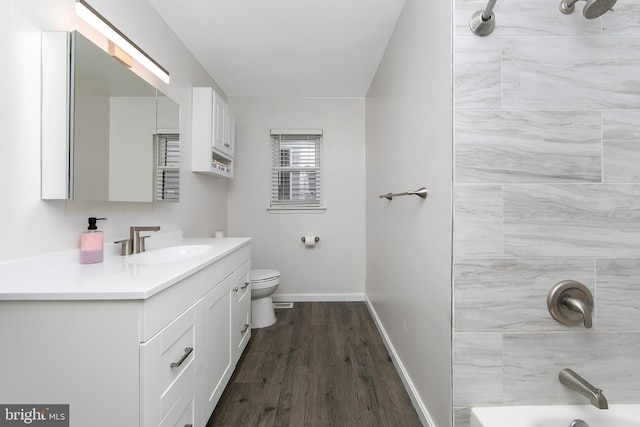 bathroom featuring toilet, vanity, wood finished floors,  shower combination, and baseboards