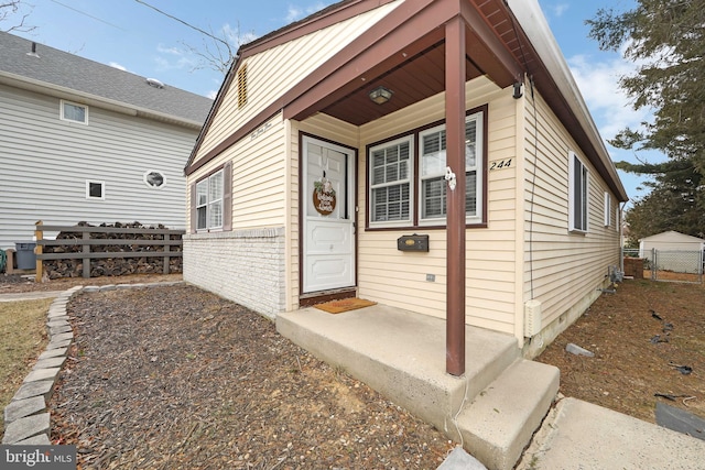 view of exterior entry featuring brick siding and fence