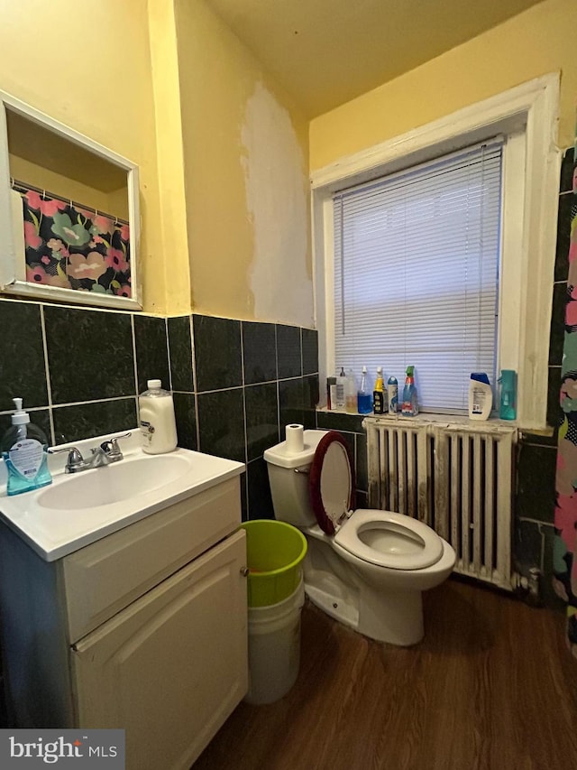 bathroom with toilet, wood finished floors, radiator heating unit, tile walls, and vanity