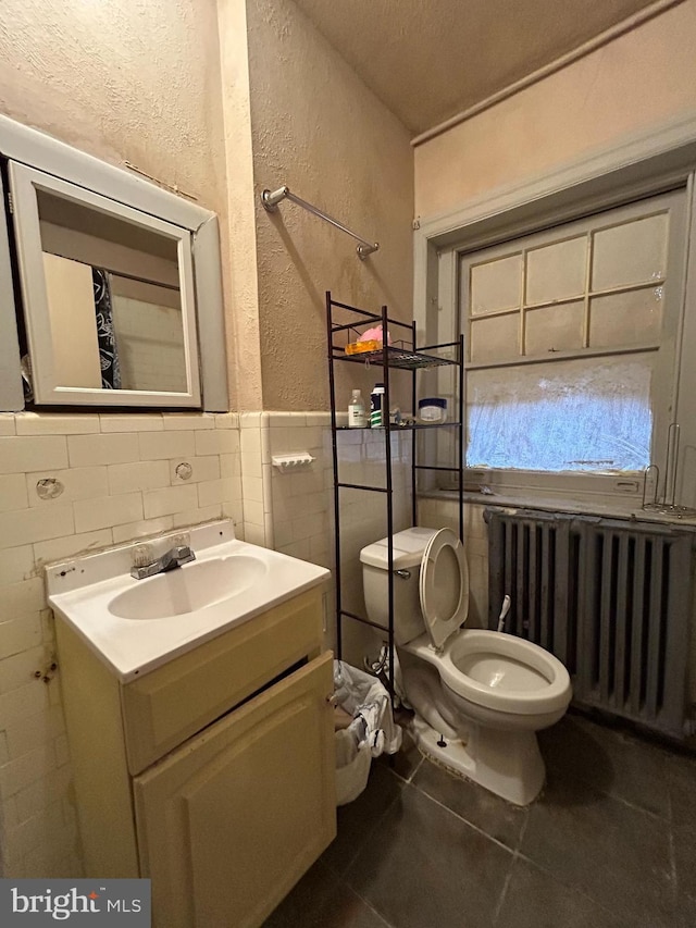 bathroom featuring toilet, radiator heating unit, tile walls, tile patterned flooring, and a textured wall