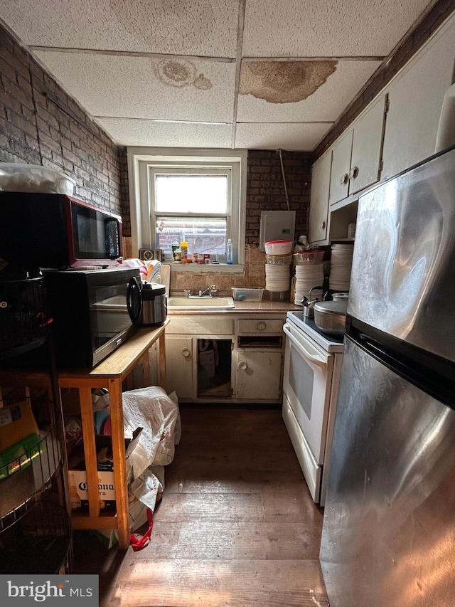 kitchen with brick wall, electric range, freestanding refrigerator, a paneled ceiling, and black microwave